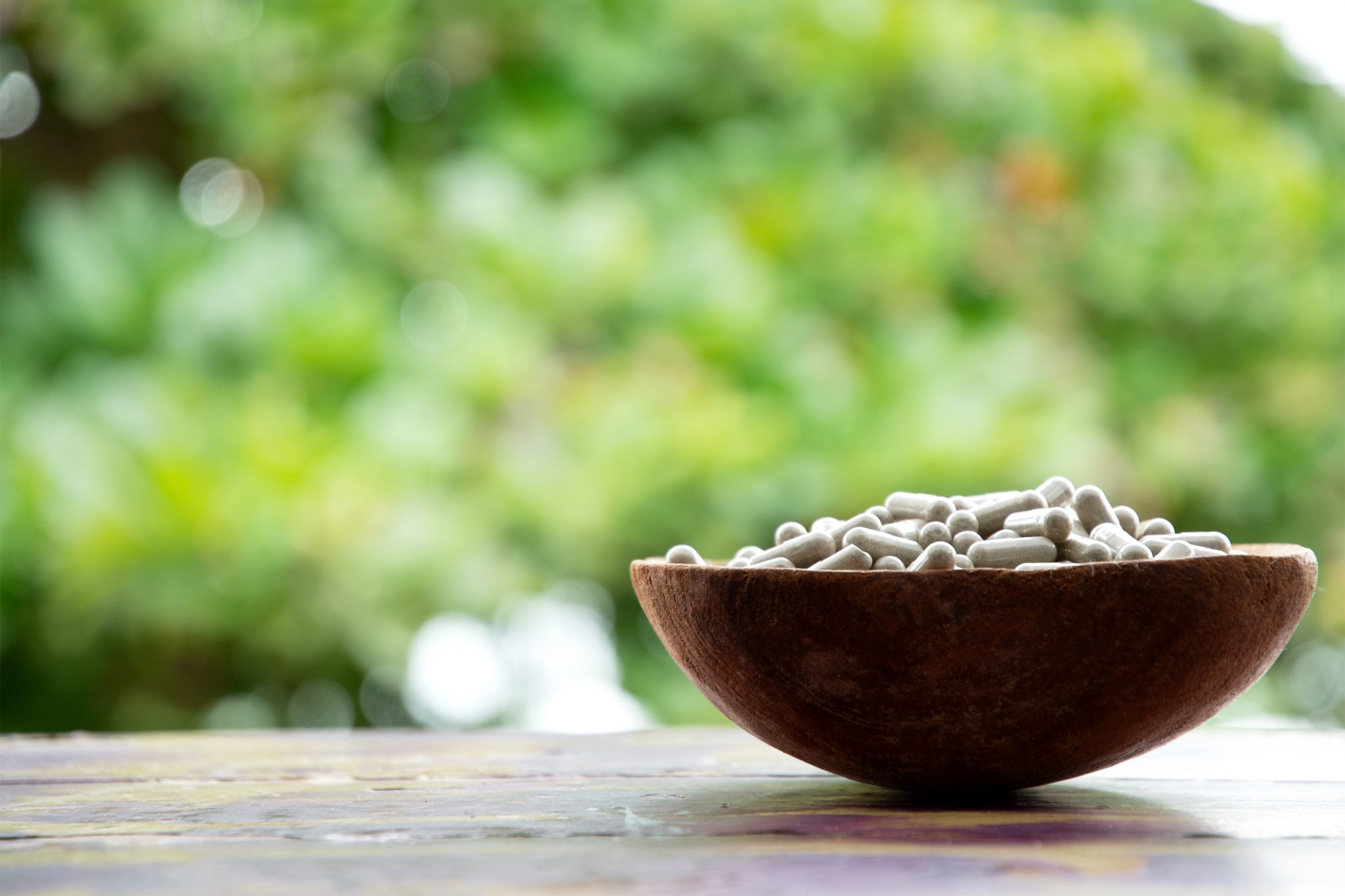 wooden bowl with encapsulated psilocybin mushroom powder with leafy, green background at mycomeditations psilocybin retreat