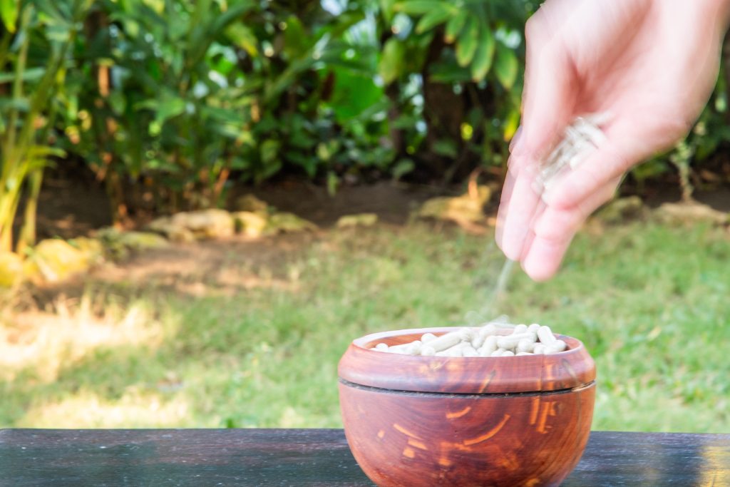 long exposure photo of hands dropping psilocybin capsules into wooden bowl on a table