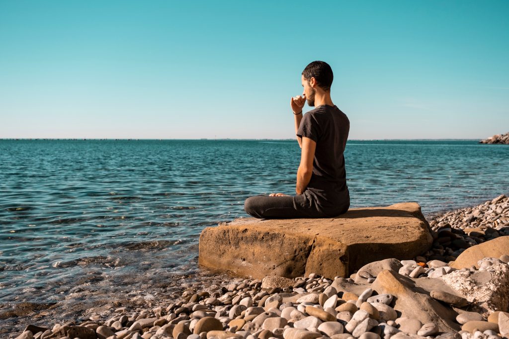 man sitting on a rock while meditating and doing breathwork