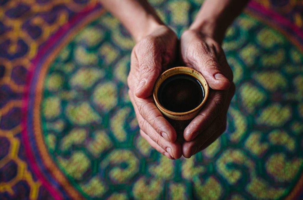 hands holding cup of ayahuasca over shipibo-styled carpet